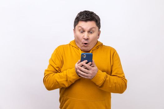 Astonished middle aged man using mobile phone with shocked expression, addicted to smartphone, texting in social network, wearing urban style hoodie. Indoor studio shot isolated on white background.