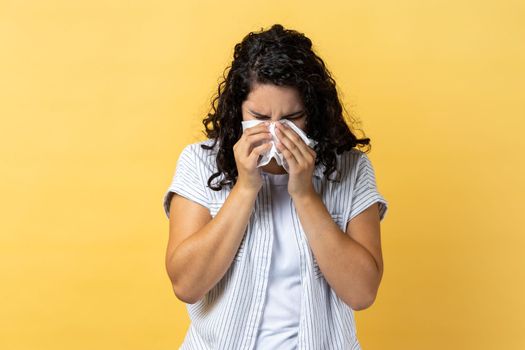 Portrait of sad frustrated woman with dark wavy hair crying and hiding face in hands, upset about loss, bereavement, feeling desperate emotion. Indoor studio shot isolated on yellow background.