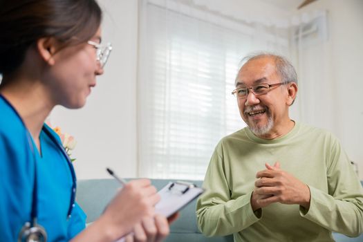 Asian young nurse writing prescription during home visit sick elder old man, Senior man takes doctor at home telling about health complaints, health care and medical concept