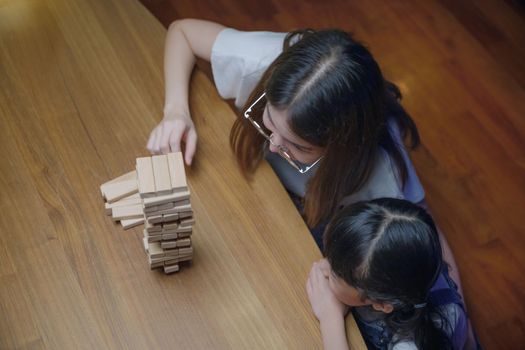 Asian young mother playing game in wood block with her little daughter in home living room at night time, Smiling woman help teach child play build constructor of wooden blocks, education