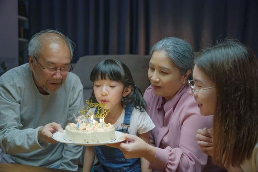 Birthday surprise. Happy Asian family grandparents and mother celebrating enjoy birthday party with cake of granddaughter at home in night time