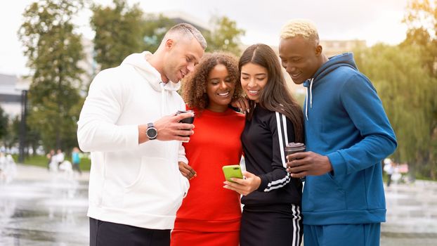 Multi-ethnic group teenage friends looking smartphone screen. African-american asian caucasian student spending time together Multiracial friendship Smiling People colorful sportswear drink coffee