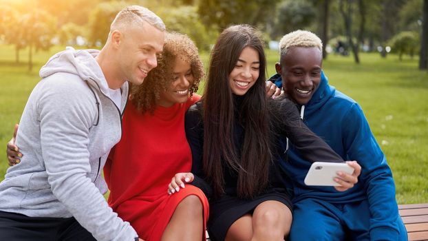 Multi ethnic friends outdoor taking a selfie on smartphone. Diverse group people Afro american asian spending time together Multiracial male female student sitting bench park outdoors