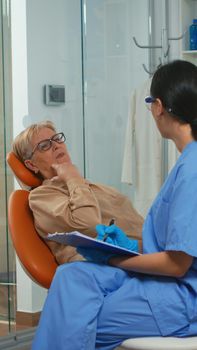 Patient with tooth pain explaining dental problem to nurse and indicating at toothache. Assistant taking notes on clipboard and preparing for stomatologic examination. Orthodontic office in modern clinic