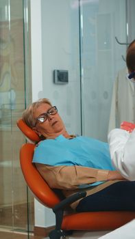 Stomatologist holding plaster model of the mandible speaking with elderly patient. Dentist showing the correct dental hygiene using mock-up of skeleton of teeth, sample of human jaw with toothbrush