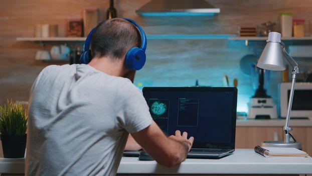 Remote man thief with headset stealing data from company hacking system from home. Programmer writing a dangerous malware for cyber attacks using performance device during midnight.