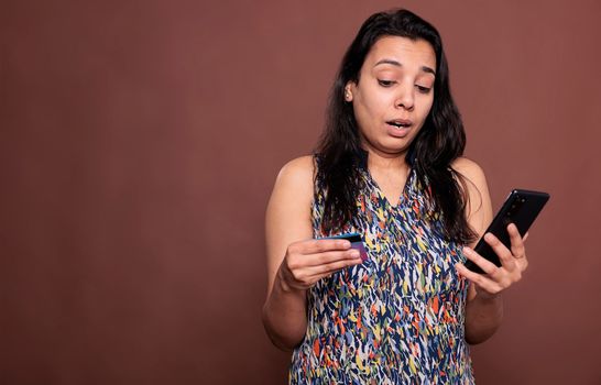 Indian woman buying product in online store, holding smartphone and credit card. Person making order in ecommerce website, searching goods in internet shop site, checkout concept