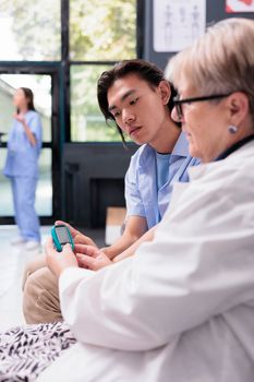 Senior physician medic measuring insulin level and glucose in blood sample using glucometer instrument, examining asian patient with diabetes. Doctor doing medical test with diabetic young adult.