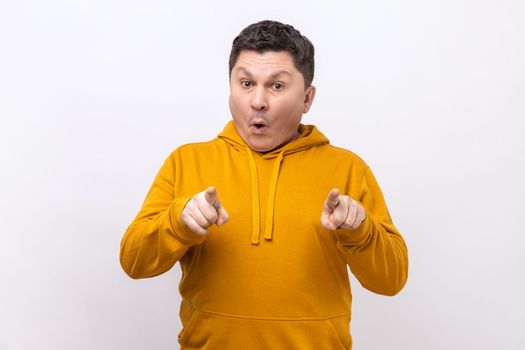 Portrait of astonished man points finger at camera and looking with shocked amazed expression, very surprised at something, wearing urban style hoodie. Indoor studio shot isolated on white background.