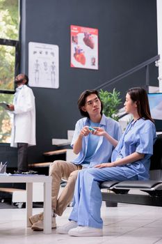 Nurse doing diabetes rutine control for asian patient using glucometer during appointment, assistant measuring glucose sugar level at insulin test. Young man having checkup visit in hospital reception