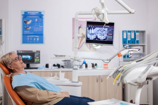 Senior woman waiting stomatolog sitting on orange chair for consultation. Elderly patient during medical examination with dentist in dental office with orange equipment.