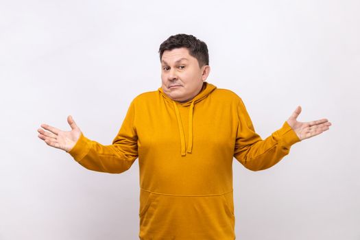 I don't know. Portrait of confused handsome young man standing with raised arms and dont know what to do, wearing urban style hoodie. Indoor studio shot isolated on white background.