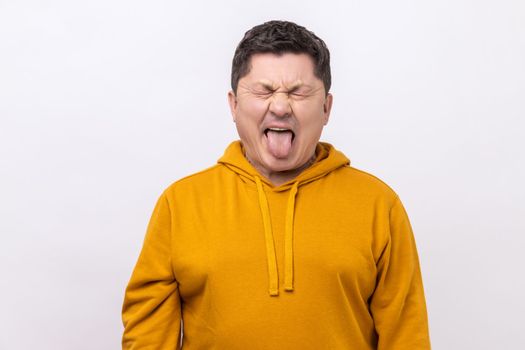 Naughty infantile middle aged man closing eyes and showing tongue, having fun, fooling around, childish manners, wearing urban style hoodie. Indoor studio shot isolated on white background.