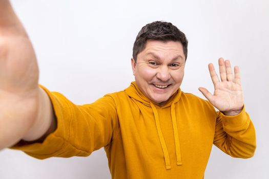 Portrait of positive handsome man making selfie or streaming, waving hand POV, point of view of photo, wearing urban style hoodie. Indoor studio shot isolated on white background.