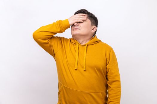 Don't want to look at this. Portrait of middle aged man covers eyes, disgust from something shameful, scared afraid to see, wearing urban style hoodie. Indoor studio shot isolated on white background.