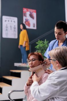 Hospital staff helping injured patient to take off neck collar, trying to recovery after fracture injury. Woman with cervical foam brace receiving help from medic and assistant in health center.