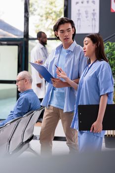 Physician nurse explaining medical expertise to asian patient after showing where need to sign before start consultation during checkup visit in hospital waiting area. Health care service and concept