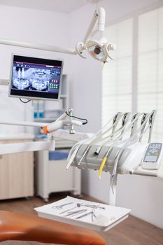 Close-up view of dental tools and professional chair at dentist. Stomatology cabinet with nobody in it and orange equipment for oral treatment.