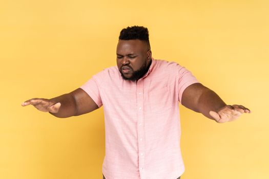 Portrait of lonely blind disabled man wearing pink shirt standing with closed eyes and outstretched hands searching way, walking with doubts. Indoor studio shot isolated on yellow background.
