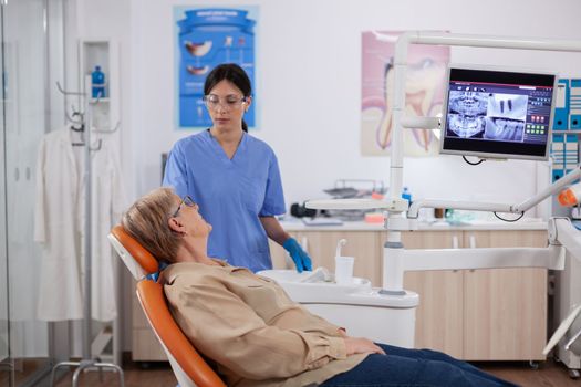 Patient having a conversation with asistant in dental clinic about oral hygiene. Senior woman talking with medical nurse in stomatology office about teeth problem.