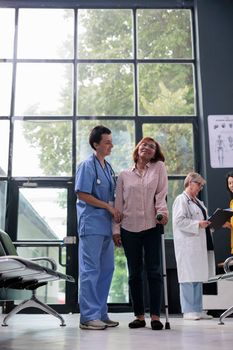 Medical assistant giving support to injured patient trying to walk with cane, using walking aid to recover after leg fracture injury. Nurse helping old woman to cure physical condition, physiotherapy.