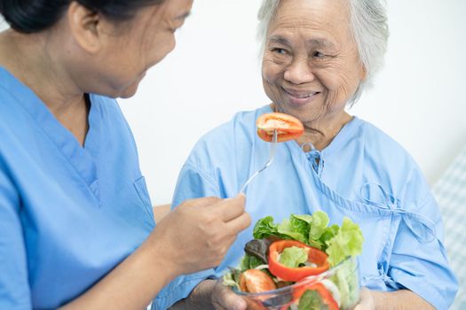 Asian senior or elderly old lady woman patient eating breakfast vegetable healthy food with hope and happy while sitting and hungry on bed in hospital.