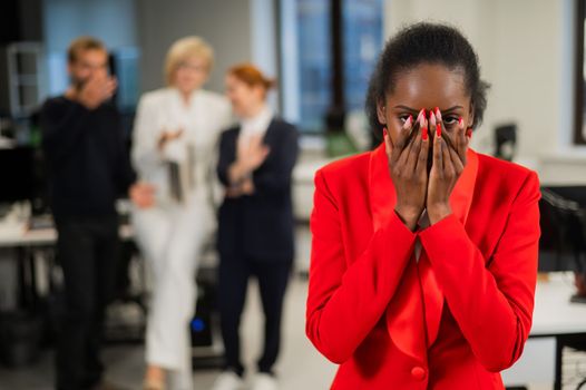 Young african woman crying because of the ridicule of colleagues. Racial discrimination in the office