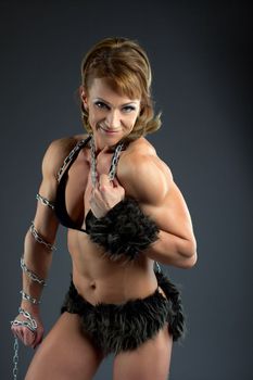 Strong athletic woman body builder posing in amazon fur costume with chain