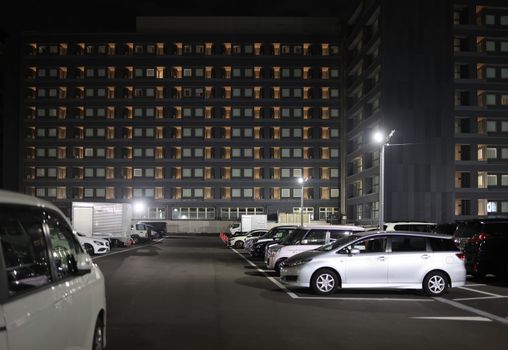 Full parking lot by multi-story building at night. High quality photo