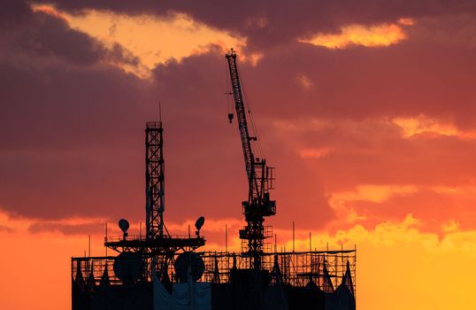 Construction crane atop unfinished building with beautiful sunset sky. High quality photo