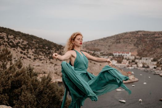 Close up shot of beautiful young caucasian woman with curly blond hair and freckles looking at camera and smiling. Cute woman portrait in a pink long dress posing on a volcanic rock high above the sea