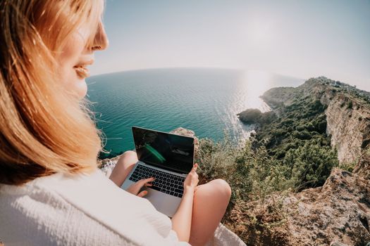 Woman sea laptop. Business woman in yellow hat working on laptop by sea. Close up on hands of pretty lady typing on computer outdoors summer day. Freelance, digital nomad, travel and holidays concept.