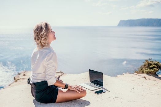 Happy girl doing yoga with laptop working at the beach. beautiful and calm business woman sitting with a laptop in a summer cafe in the lotus position meditating and relaxing. freelance girl remote work beach paradise