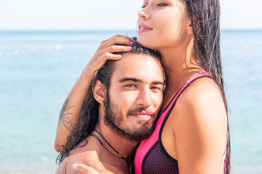 Close up shot of beautiful young caucasian woman with black hair and freckles looking at camera and smiling. Cute woman portrait in a pink bikini posing on a volcanic rock high above the sea