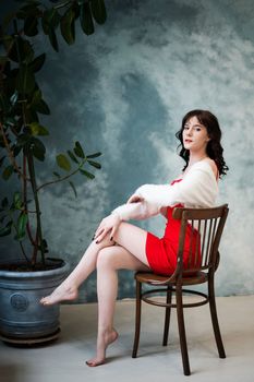 Caucasian brunette woman sits on a wooden chair against a gray wall background