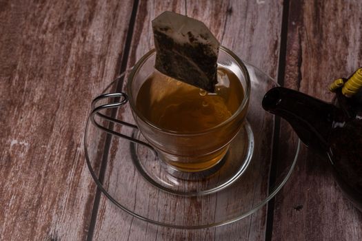 tea cup and teapot pouring hot tea on a wooden table and black background with copy-space