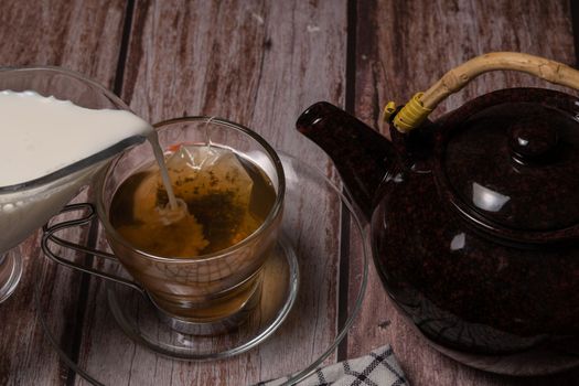 tea cup and teapot pouring hot tea on a wooden table and black background with copy-space