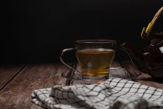 tea cup and teapot pouring hot tea on a wooden table and black background with copy-space