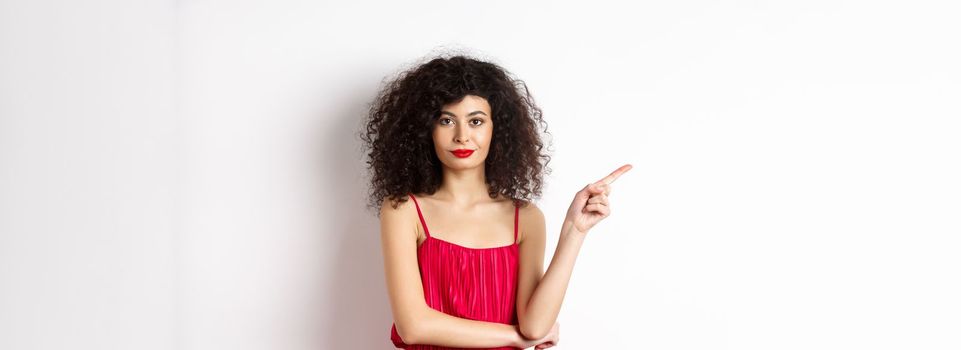 Attractive lady in red dress and makeup pointing finger left, showing logo, standing over white background.