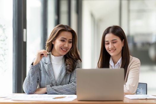 Working together on project. Two young asian business colleagues working on laptop computer