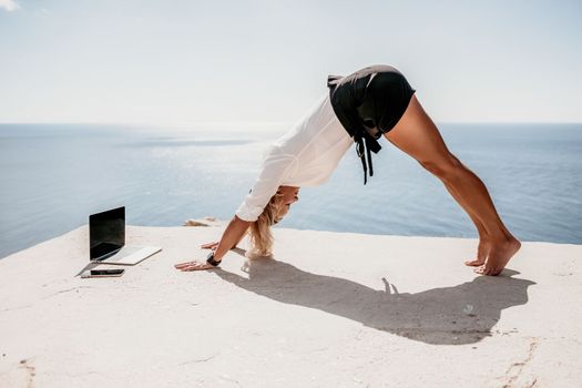 Happy girl doing yoga with laptop working at the beach. beautiful and calm business woman sitting with a laptop in a summer cafe in the lotus position meditating and relaxing. freelance girl remote work beach paradise