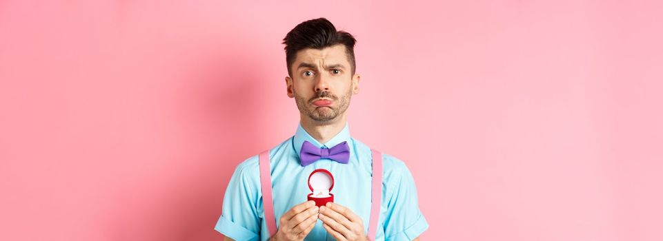 Valentines day. Sad boyfriend being rejected, showing engagement ring and sulking upset, she said no, standing over pink background.