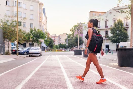 latina female athlete walking with backpack on a city running track, urban sport and healthy lifestyle concept, copy space for text