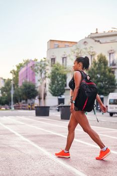 vertical photo of a latina sportswoman walking with a backpack on a city athletics track, urban sport and healthy lifestyle concept, copy space for text