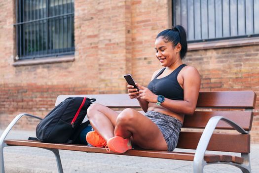 smiling sportswoman using her mobile phone before her workout, urban sports and healthy lifestyle concept, copy space for text
