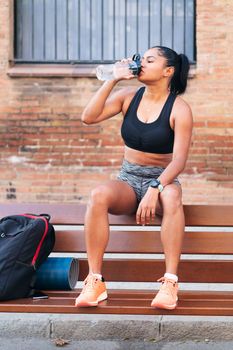 latin sportswoman drinking water during a break in her workout, urban sports and healthy lifestyle concept