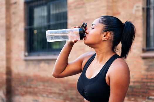 portrait of a sportswoman drinking water during a break in her workout, urban sports and healthy lifestyle concept