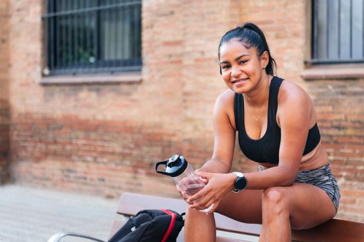 latin sportswoman with a bottle of water smiling looking at camera, urban sports and healthy lifestyle concept, copy space for text