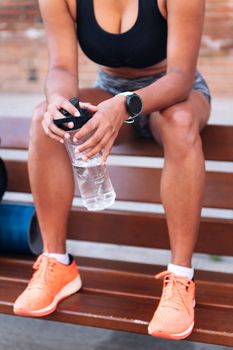 detail of the hands of an unrecognizable sportswoman holding a bottle of water while resting on a bench during a break in her training, urban sport and healthy lifestyle concept