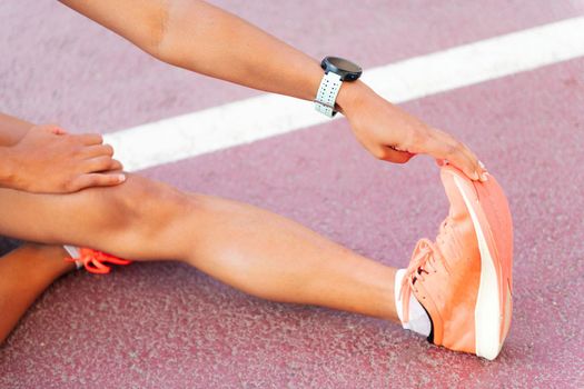 detail of the leg of a female athlete stretching sitting on the athletics track, concept of urban sport and healthy lifestyle